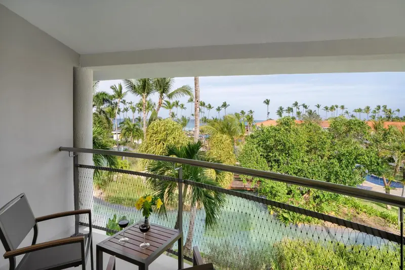 Une terrasse avec une table basse et des fauteuils offre une vue sur la végétation et la mer.