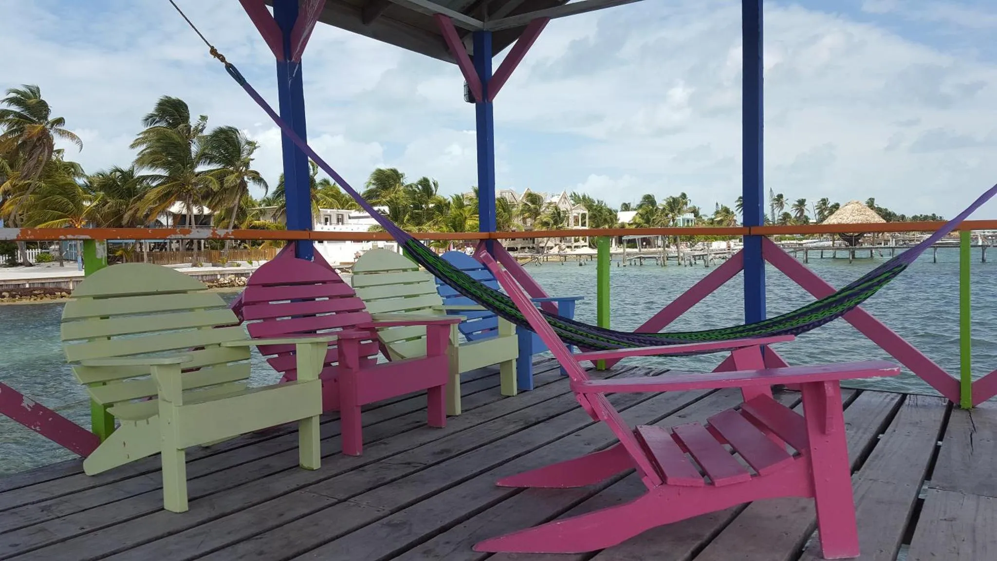 Deux chaises longues colorées et un hamac sont installés sur une terrasse en bois face à la mer.