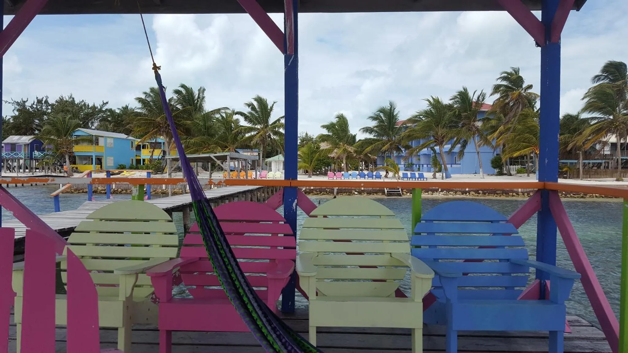 Des fauteuils colorés et un hamac sont disposés sur une terrasse en bois face à la mer.