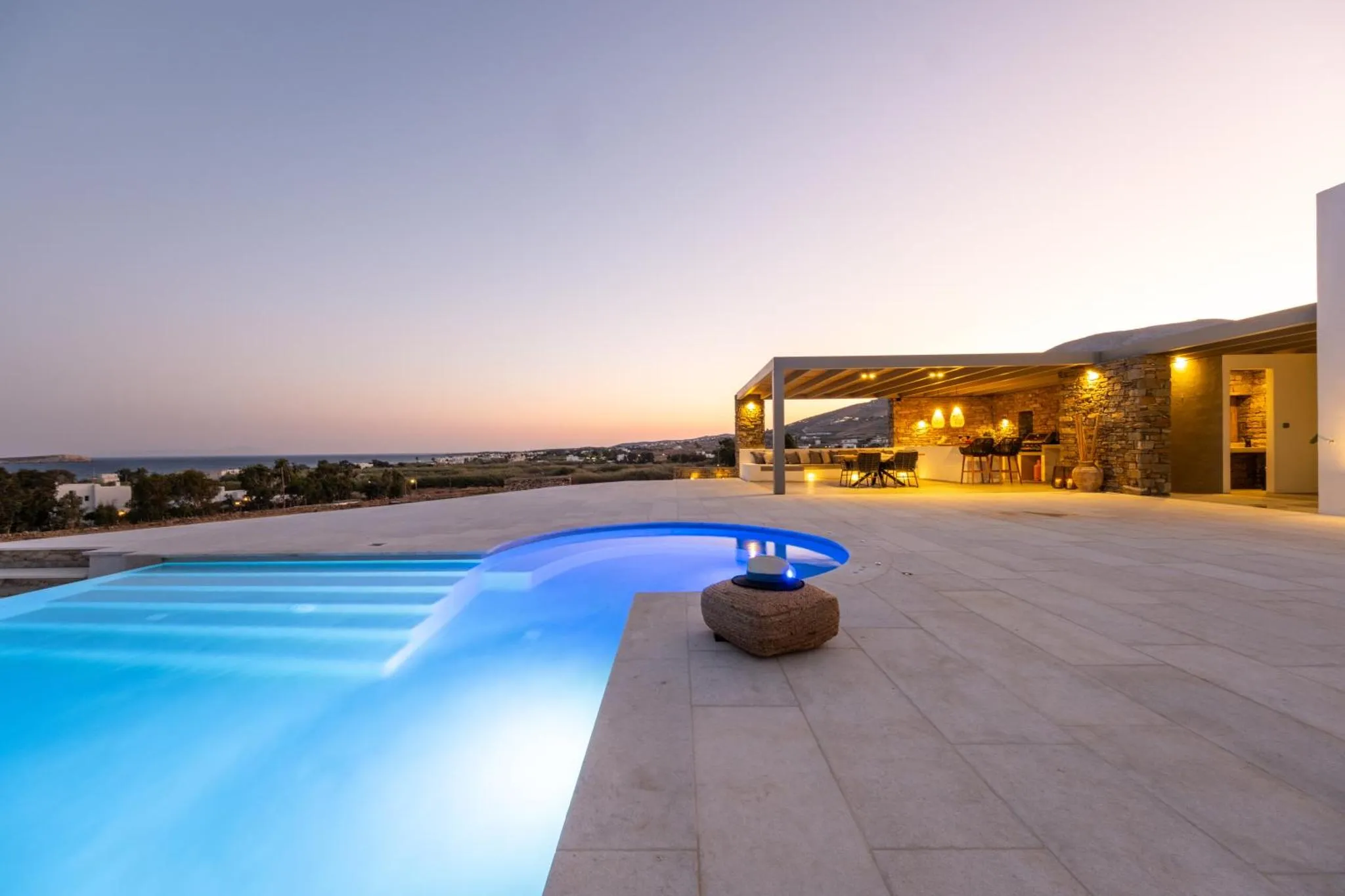 Terrasse lumineuse avec piscine et vue sur la mer au coucher du soleil.