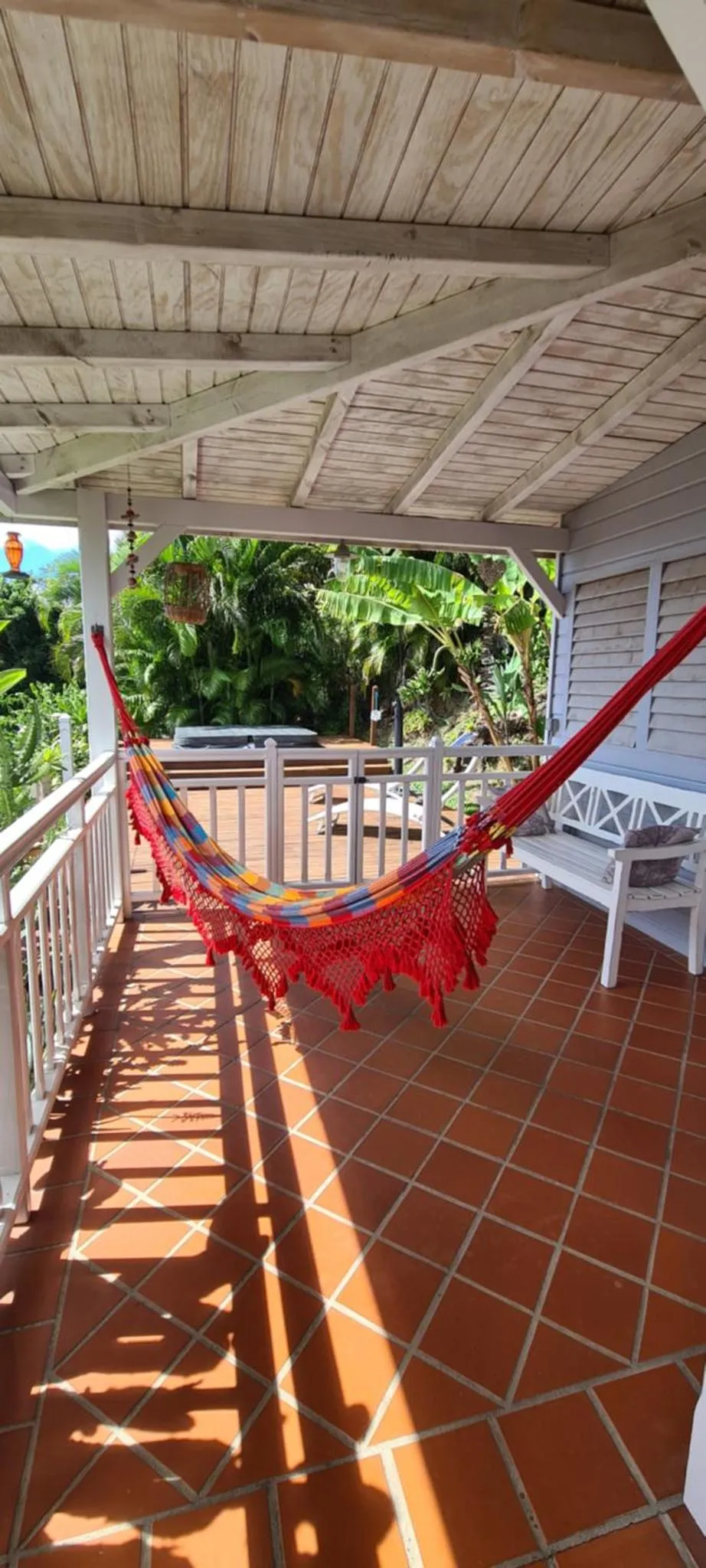 Un hamac coloré est suspendu sur une terrasse carrelée et ombragée.