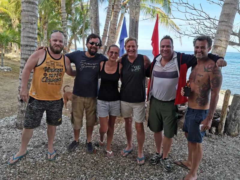 Groupe de personnes souriantes posant sur une plage ensoleillée.