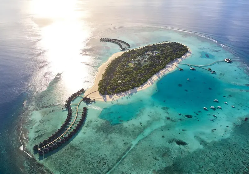 Vue aérienne d'une île tropicale avec des bungalows sur pilotis et une plage de sable blanc.