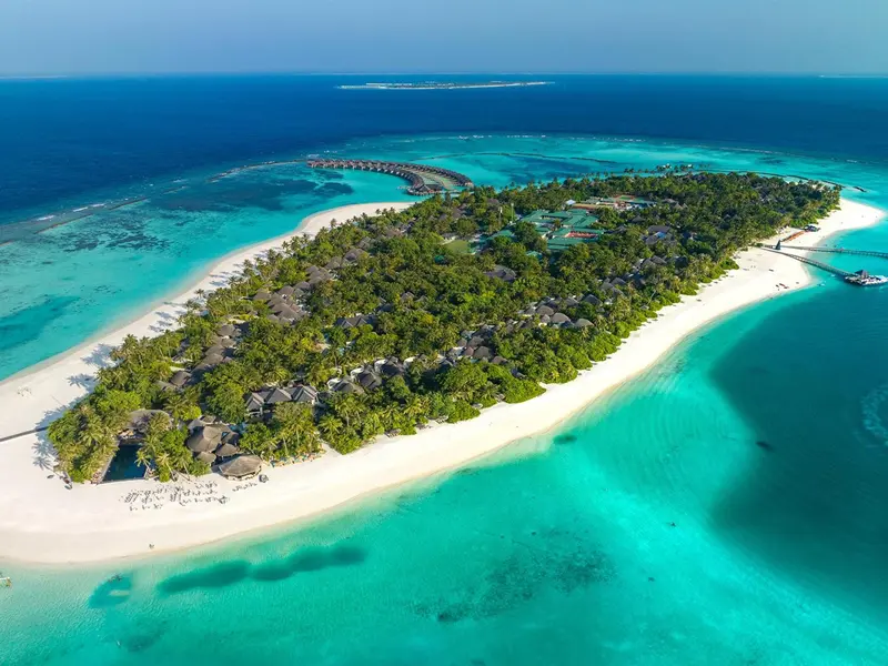 Vue aérienne d'une île tropicale avec des bungalows sur pilotis et une plage de sable blanc.