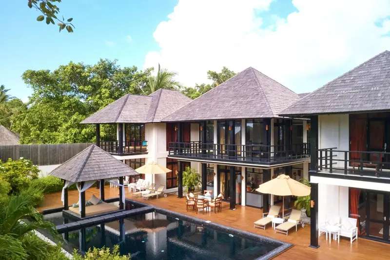 Bâtiments blancs aux toits de chaume surplombent une piscine et une terrasse.