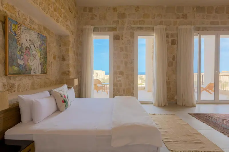 Une chambre lumineuse avec un grand lit blanc et vue sur la mer.