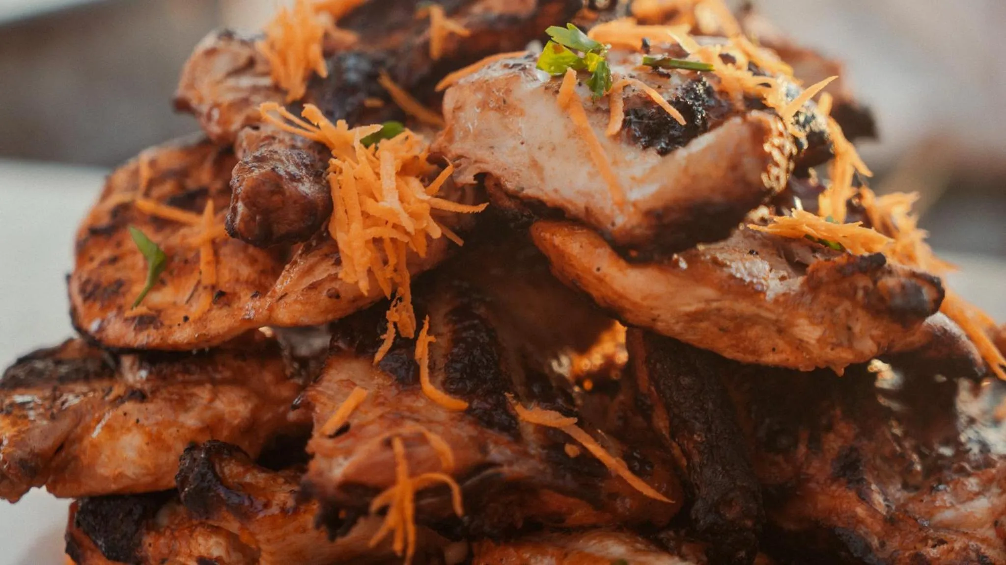 Une pile de morceaux de poulet grillés est garnie de zestes d'orange et de verdure.