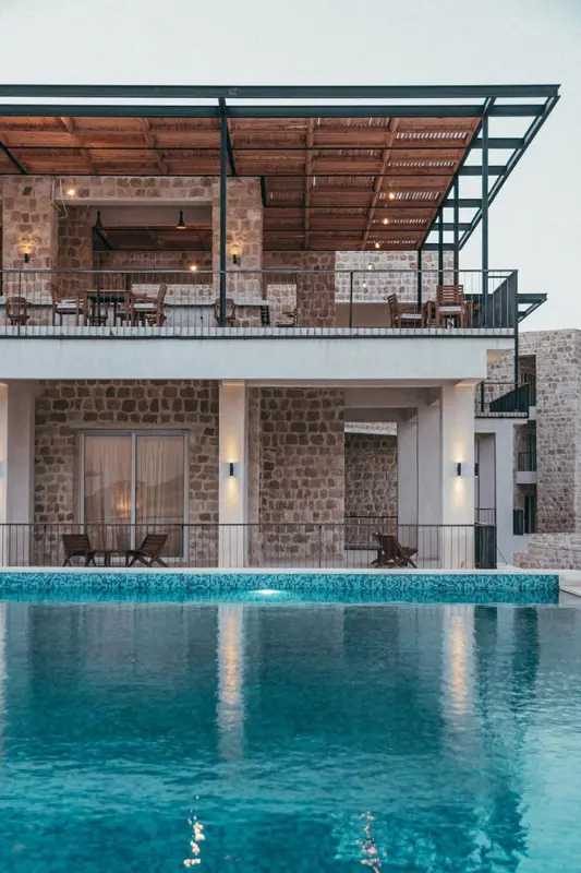 Façade en pierre d'un bâtiment avec une piscine au premier plan et des balcons à l'étage.