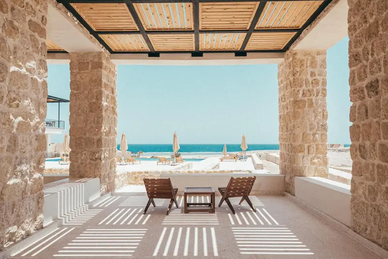 Terrasse ombragée donnant sur une plage de sable fin et une mer turquoise.