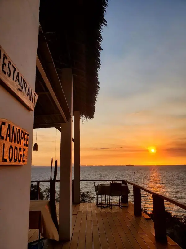 Terrasse en bois avec mobilier d'extérieur donnant sur une mer au coucher du soleil.