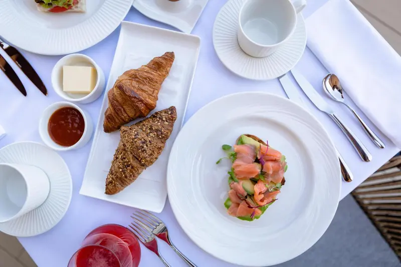 Une table blanche est dressée avec un petit-déjeuner composé de viennoiseries, de confiture et de toasts.