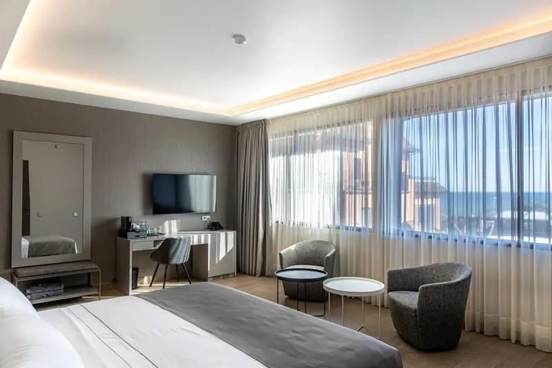 Chambre lumineuse avec un grand lit et un coin salon près d'une fenêtre.