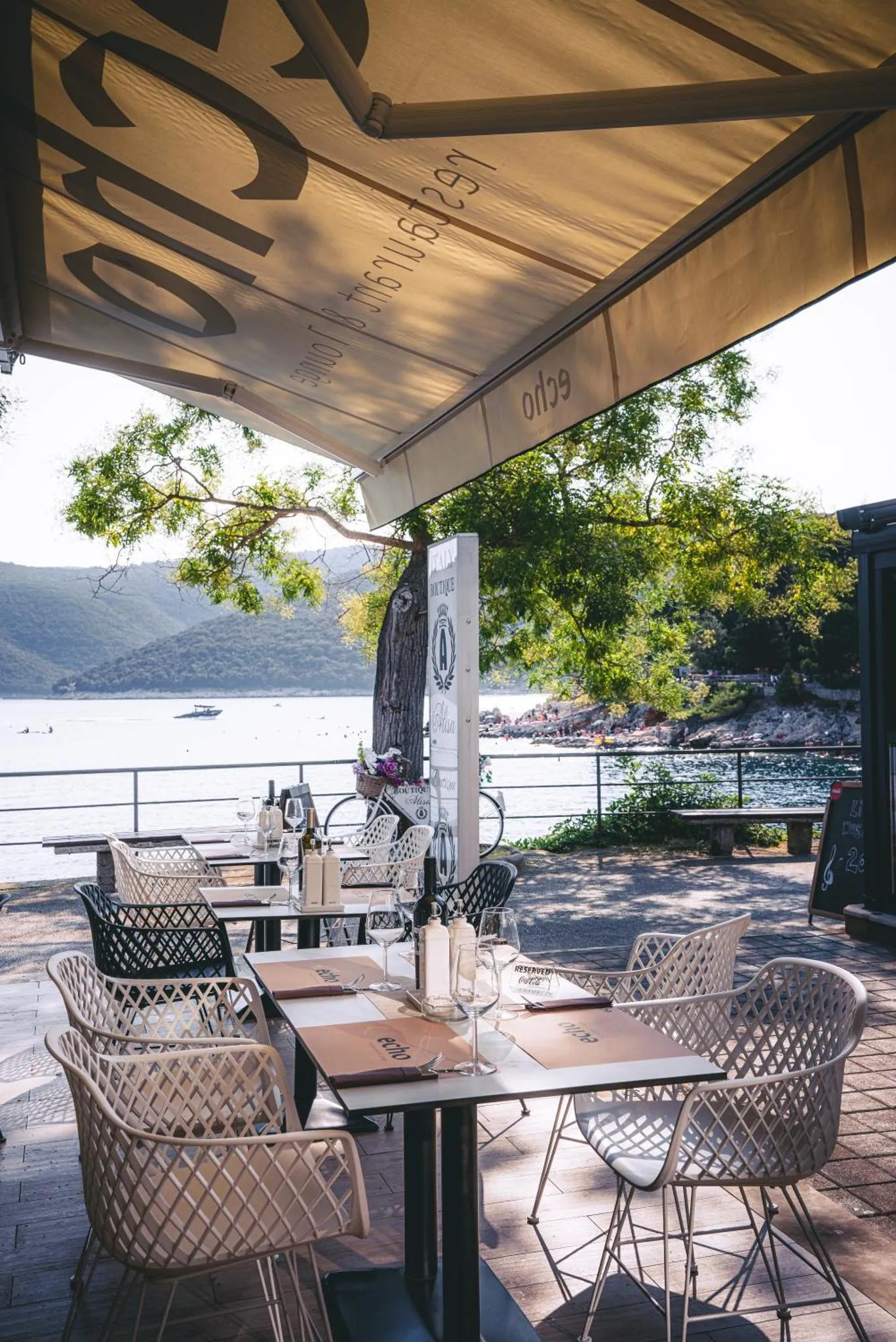 Tables et chaises disposées sur une terrasse ombragée avec vue sur la mer.