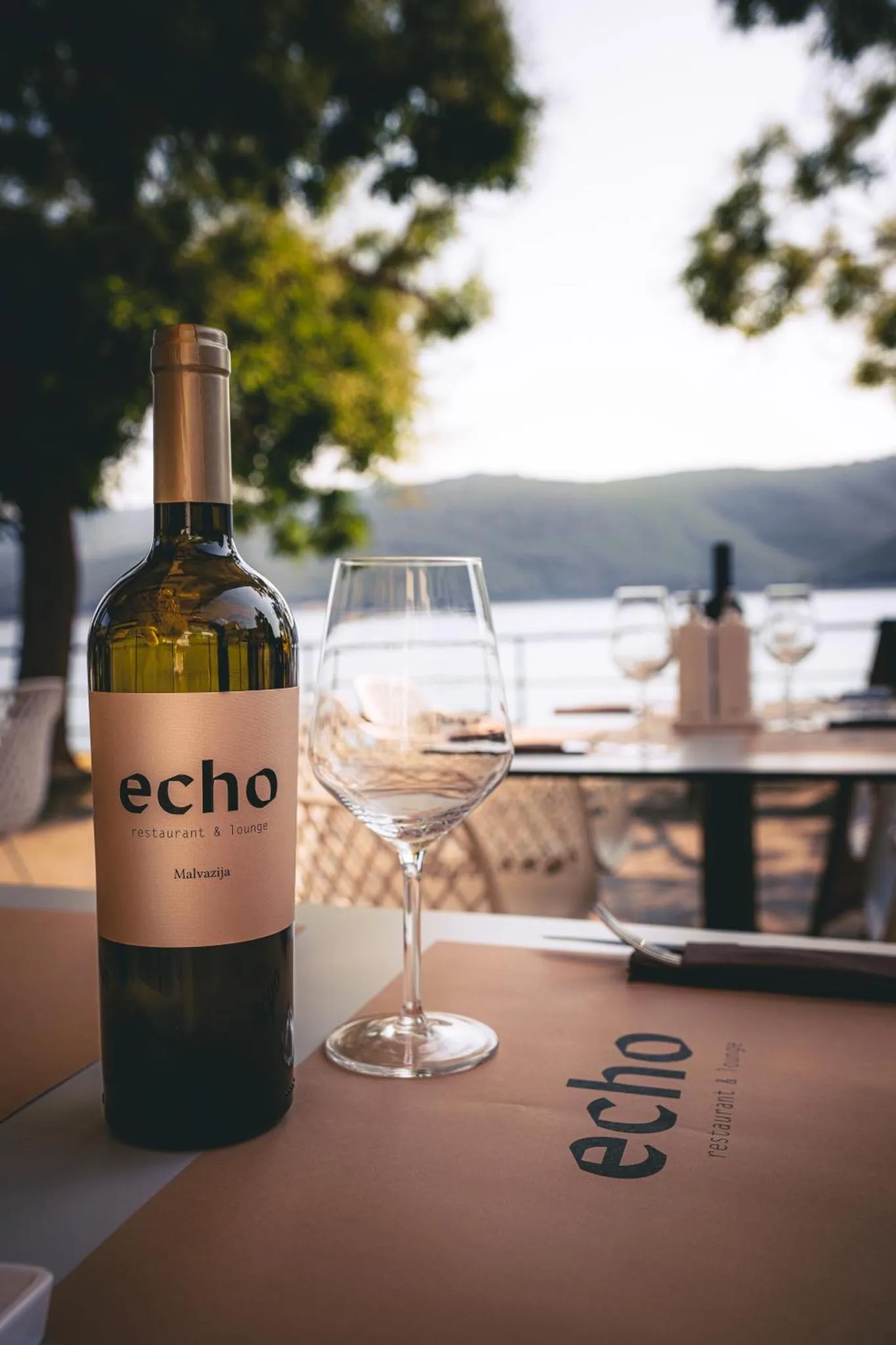 Une bouteille de vin et un verre sur une table en terrasse avec vue sur la mer.