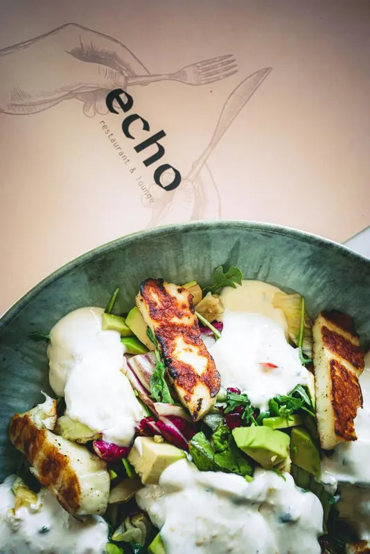 Salade colorée avec du fromage grillé et une sauce crémeuse présentée dans un saladier métallique.