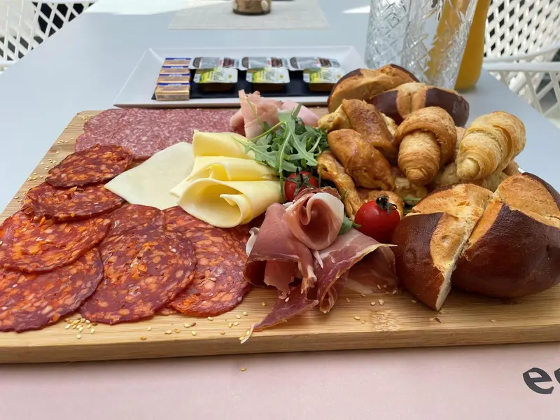 Assortiment de charcuterie, fromages et viennoiseries présentés sur une planche en bois.