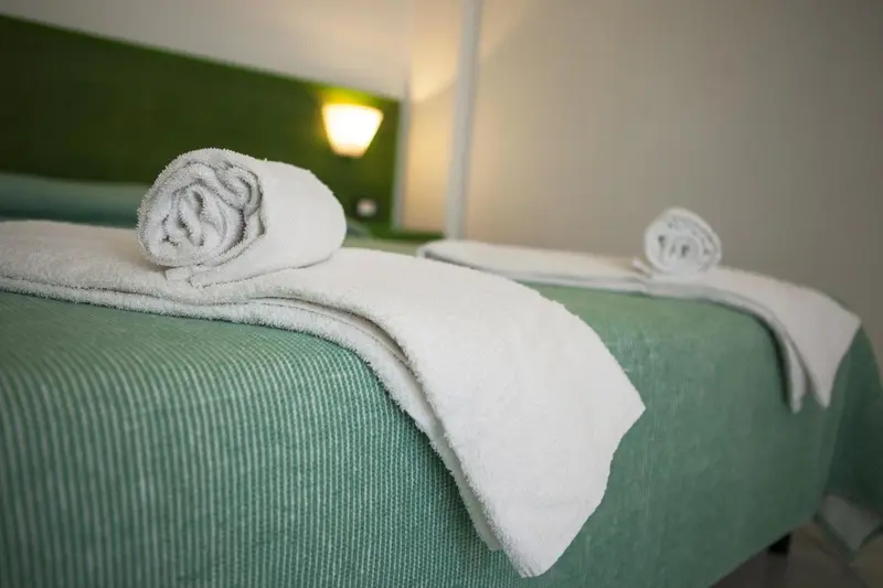 Un lit avec des draps verts et des serviettes blanches roulées.