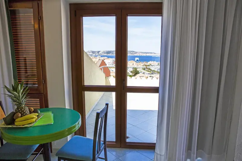 Une table verte et des chaises se trouvent devant des portes ouvertes donnant sur une vue sur la mer.