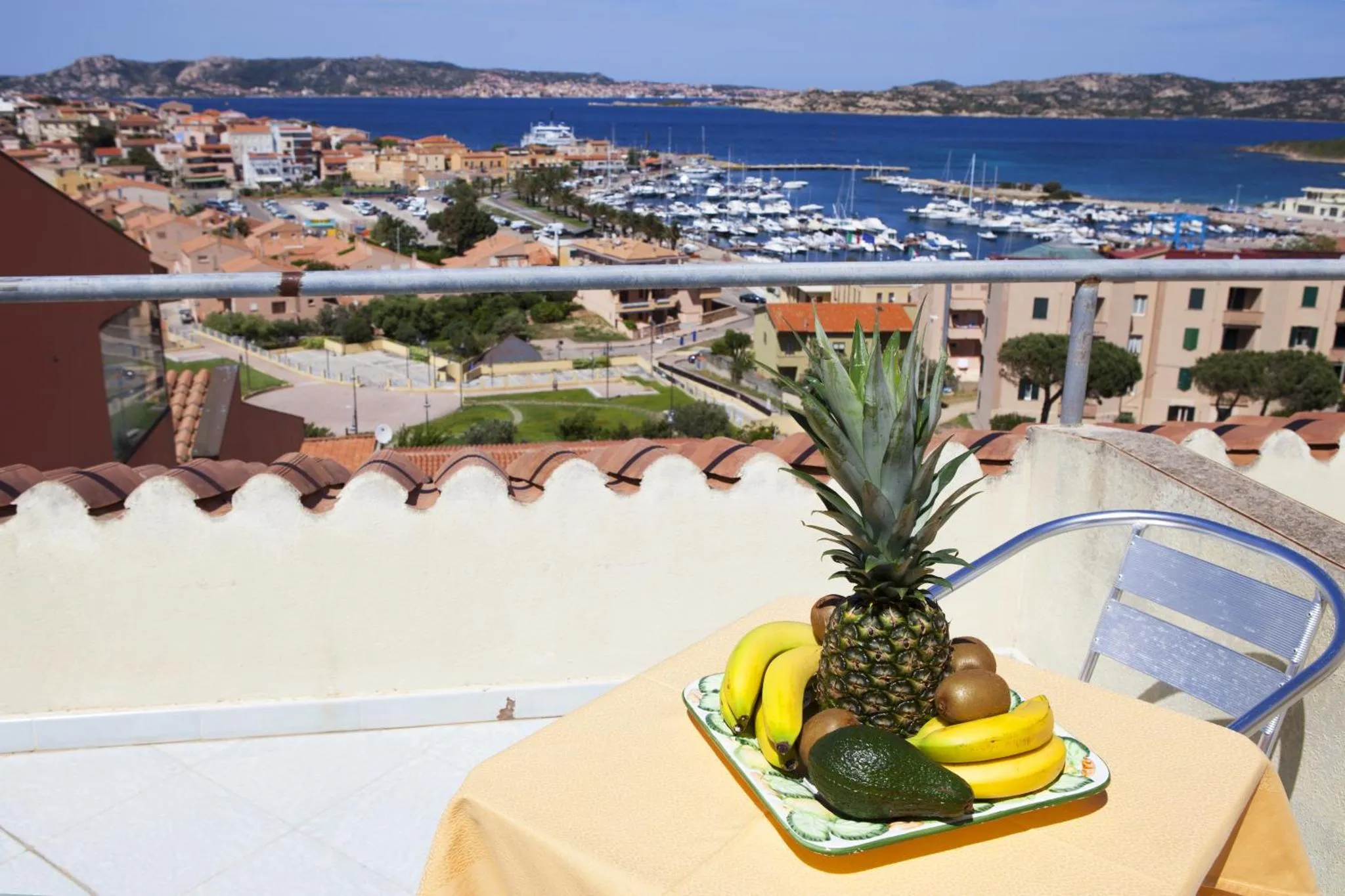 Une table avec des fruits frais sur une terrasse ensoleillée avec vue sur la mer et un port de plaisance.