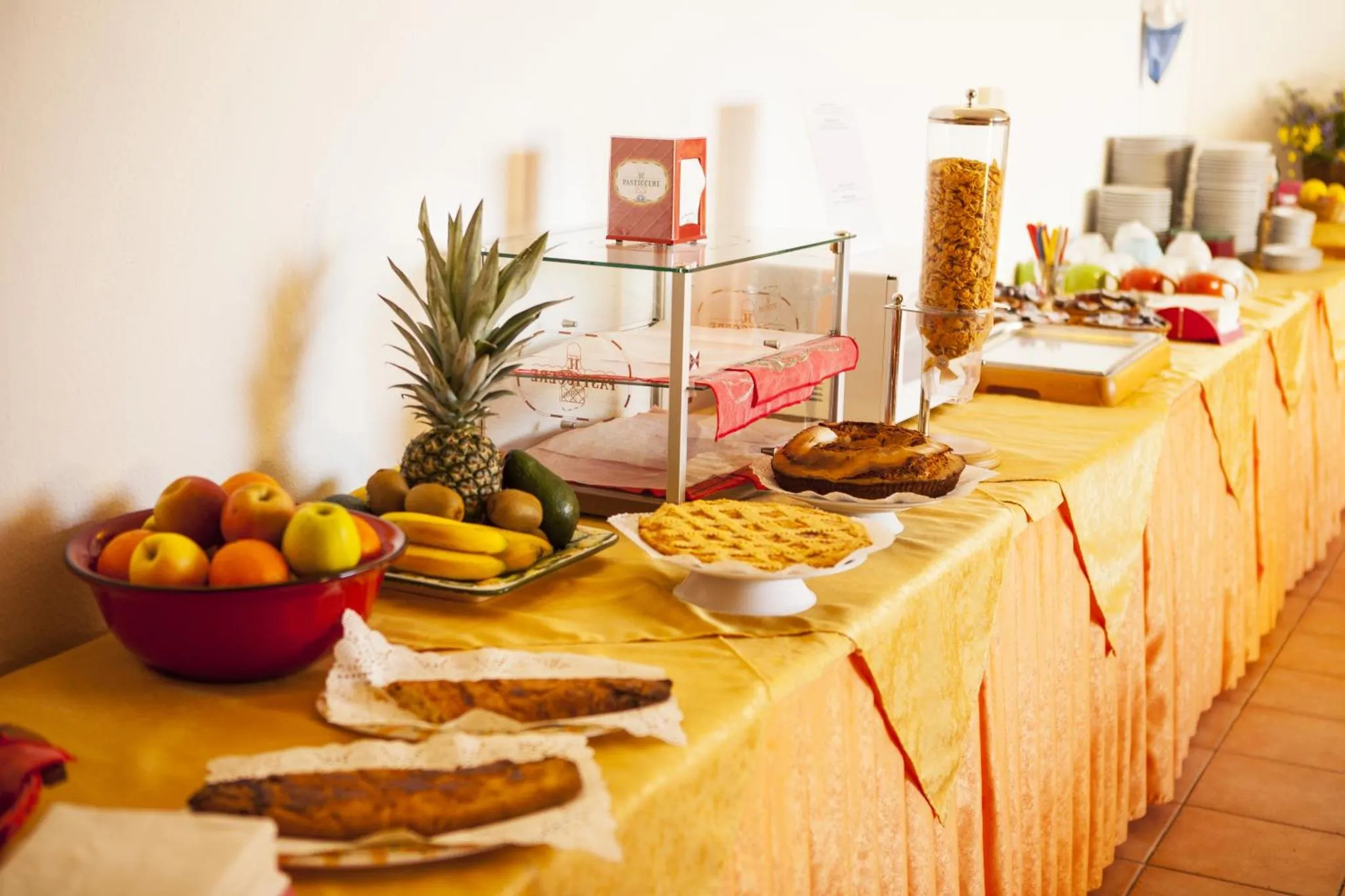 Un buffet propose des fruits frais et des pâtisseries sur une table recouverte d'une nappe jaune.
