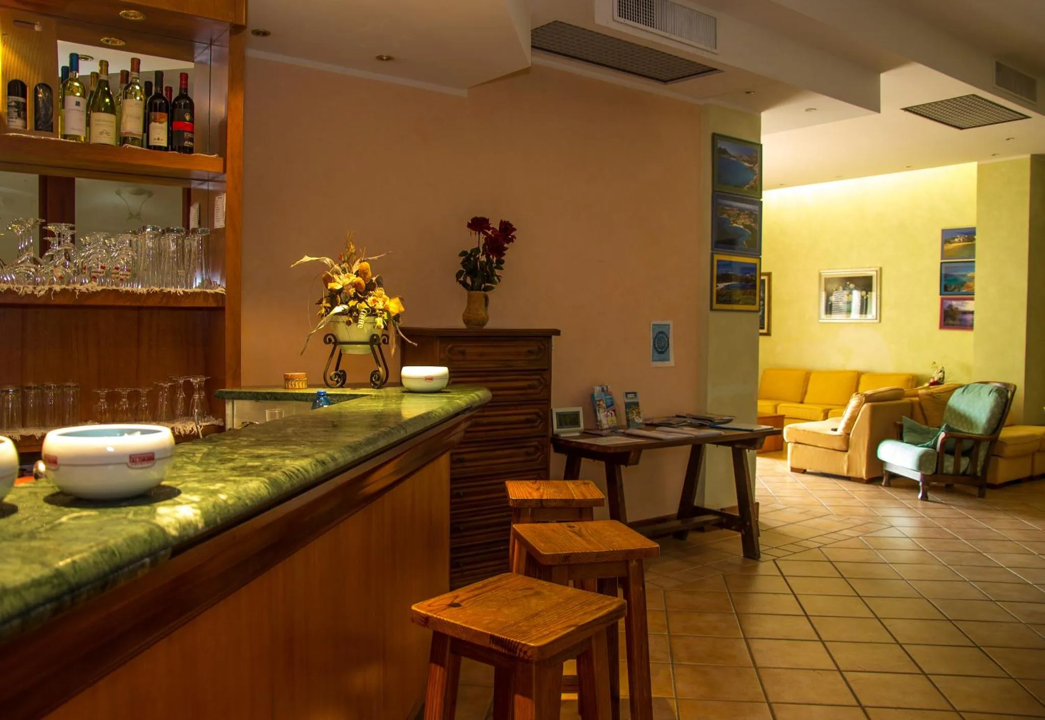 Un comptoir de bar en bois avec des bouteilles et des verres, et des tables basses dans un espace de détente.
