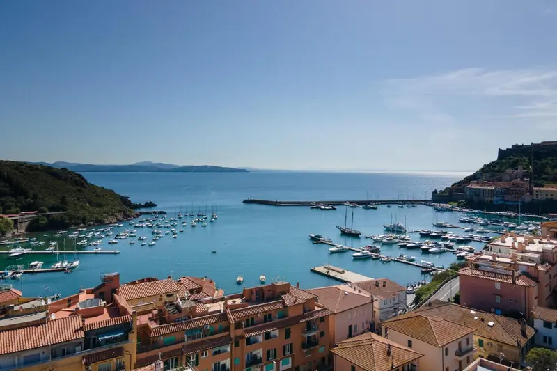 Vue aérienne d'un port de plaisance bordé de bâtiments aux toits rouges et d'une côte rocheuse.