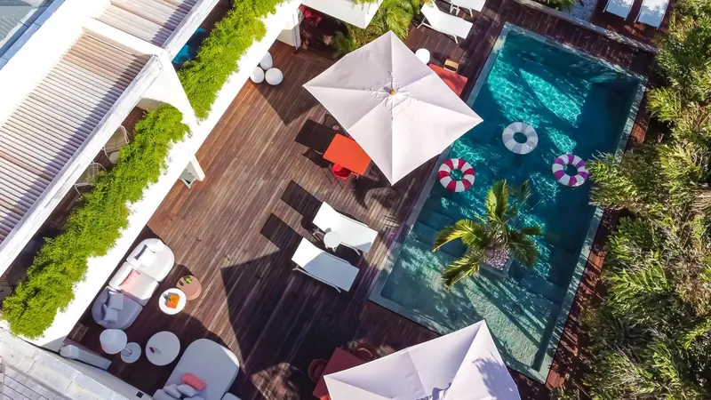 Terrasse en bois avec transats blancs et parasols au bord d'une piscine.
