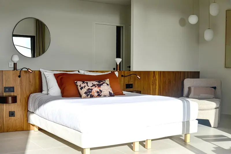 Une chambre lumineuse avec un grand lit recouvert d'une courtepointe blanche et de coussins colorés.