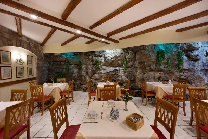 Une salle de restaurant avec des tables nappées et un décor mural imitant des rochers.