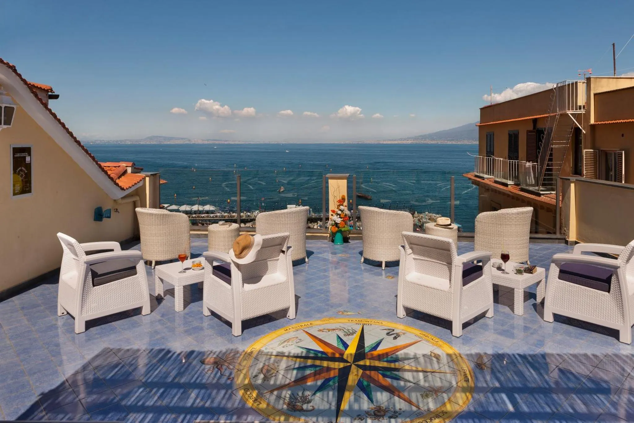 Terrasse aménagée avec mobilier blanc offrant une vue sur la mer et les montagnes.