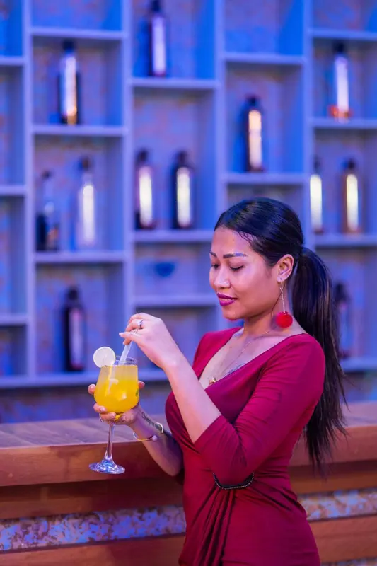 Une serveuse prépare un cocktail derrière un comptoir illuminé.