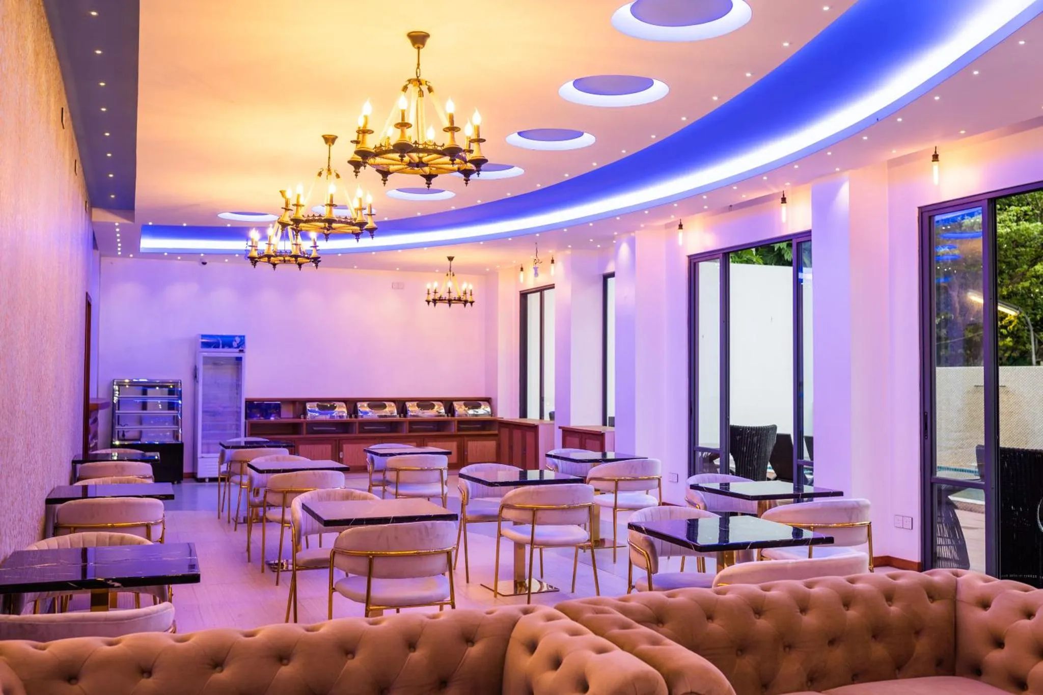 Une salle lumineuse avec des tables et des chaises dorées, éclairée par des lustres et des lumières bleues.