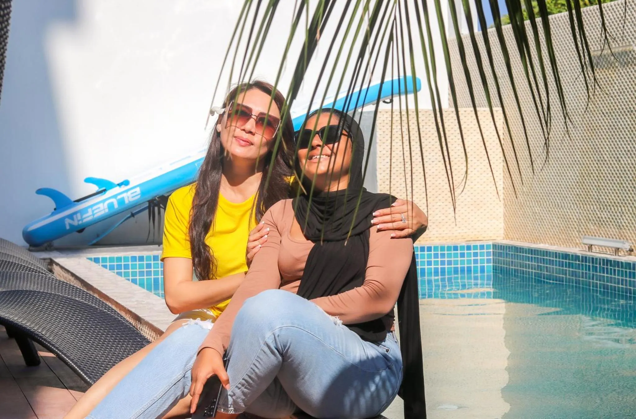 Deux femmes souriantes se reposent au bord d'une piscine ensoleillée.