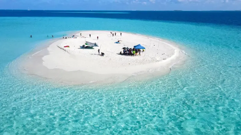 Une île de sable blanc entourée d'eau turquoise, avec des parasols et des personnes.