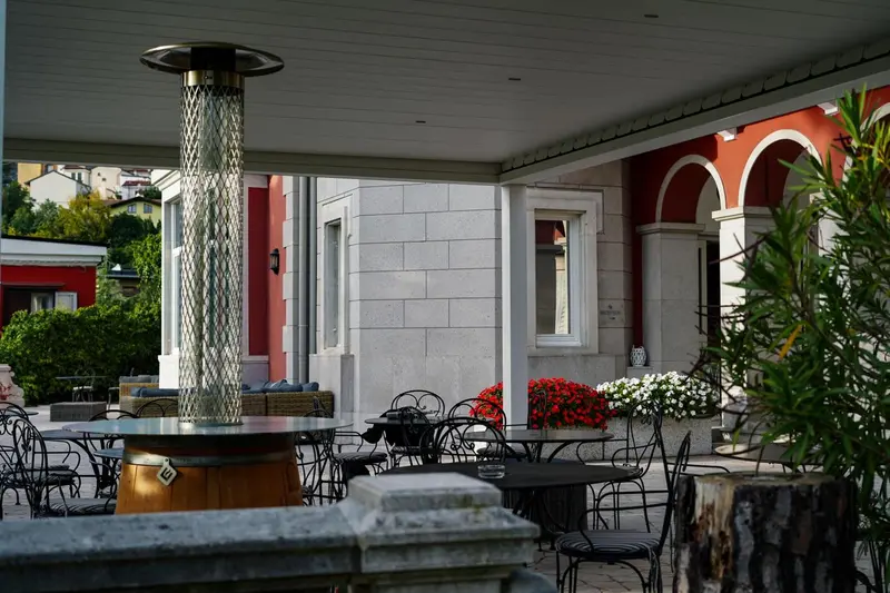 Terrasse ombragée avec tables et chaises, agrémentée de plantes et d'un chauffage d'extérieur.