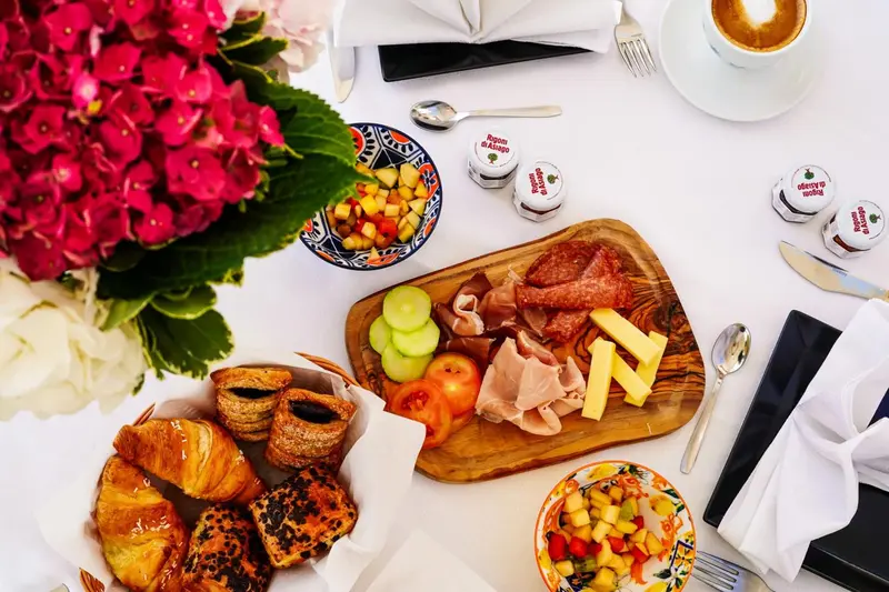 Une table est dressée avec un petit-déjeuner composé de viennoiseries, de fruits, de charcuterie et de boissons.