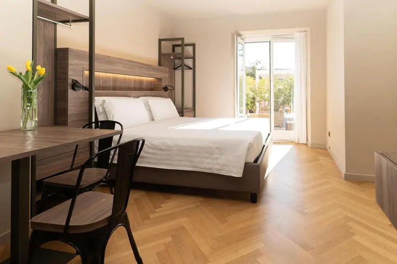 Une chambre lumineuse avec un lit double et un coin repas près d'une baie vitrée.
