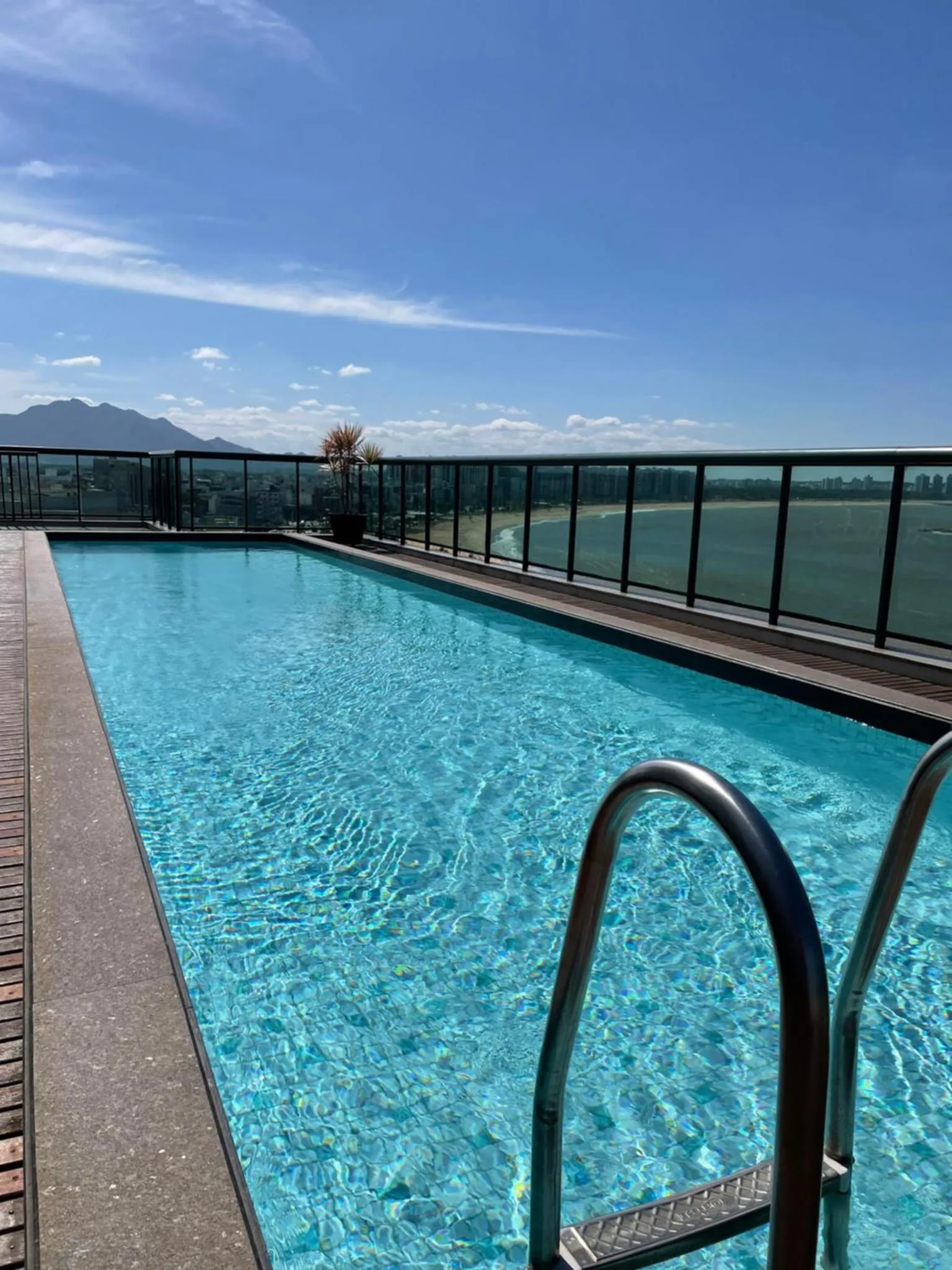 Une piscine rectangulaire avec des escaliers en acier inoxydable, entourée d'une terrasse et offrant une vue sur un paysage montagneux.