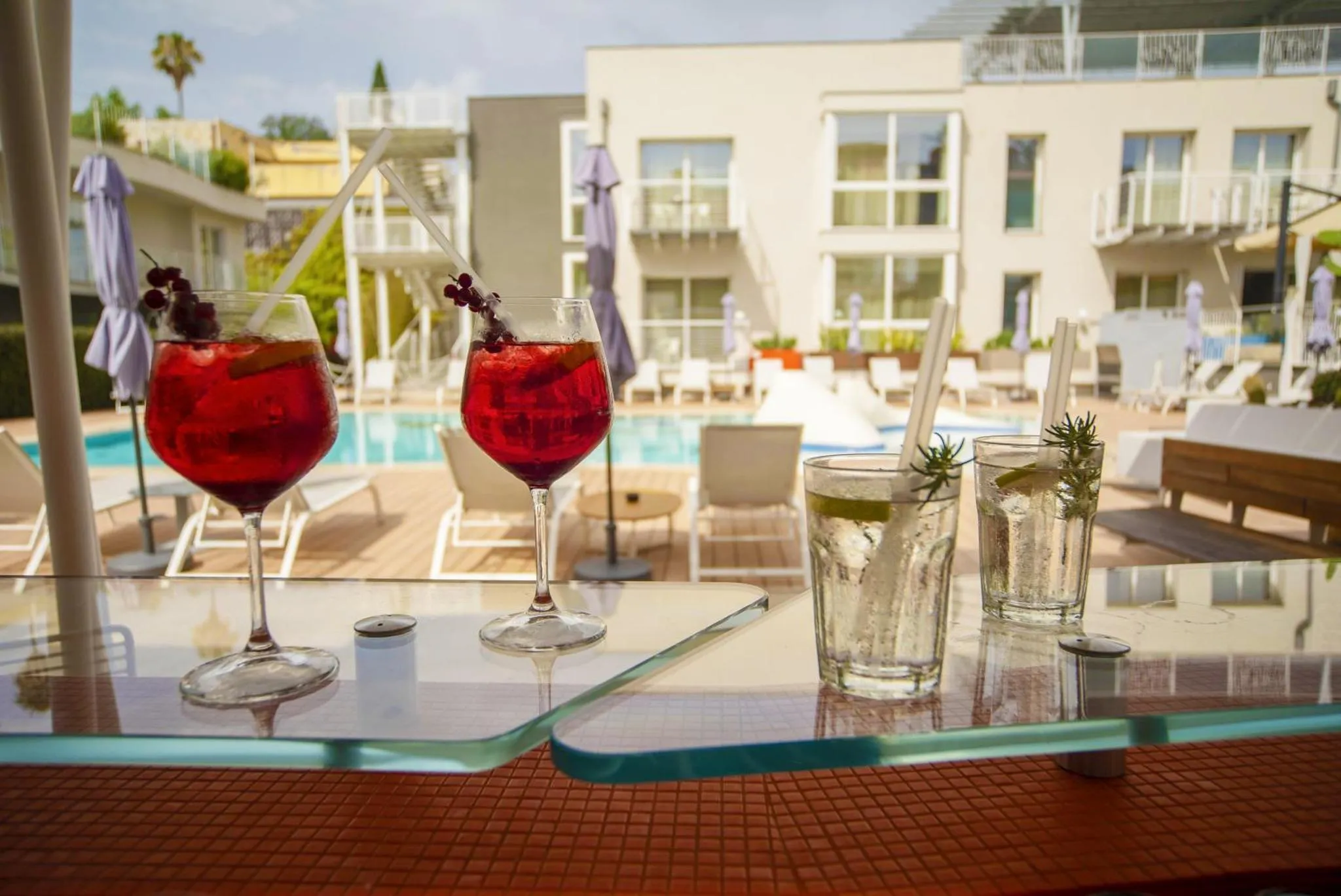 Deux cocktails colorés et des boissons fraîches sur une table près d'une piscine ensoleillée.