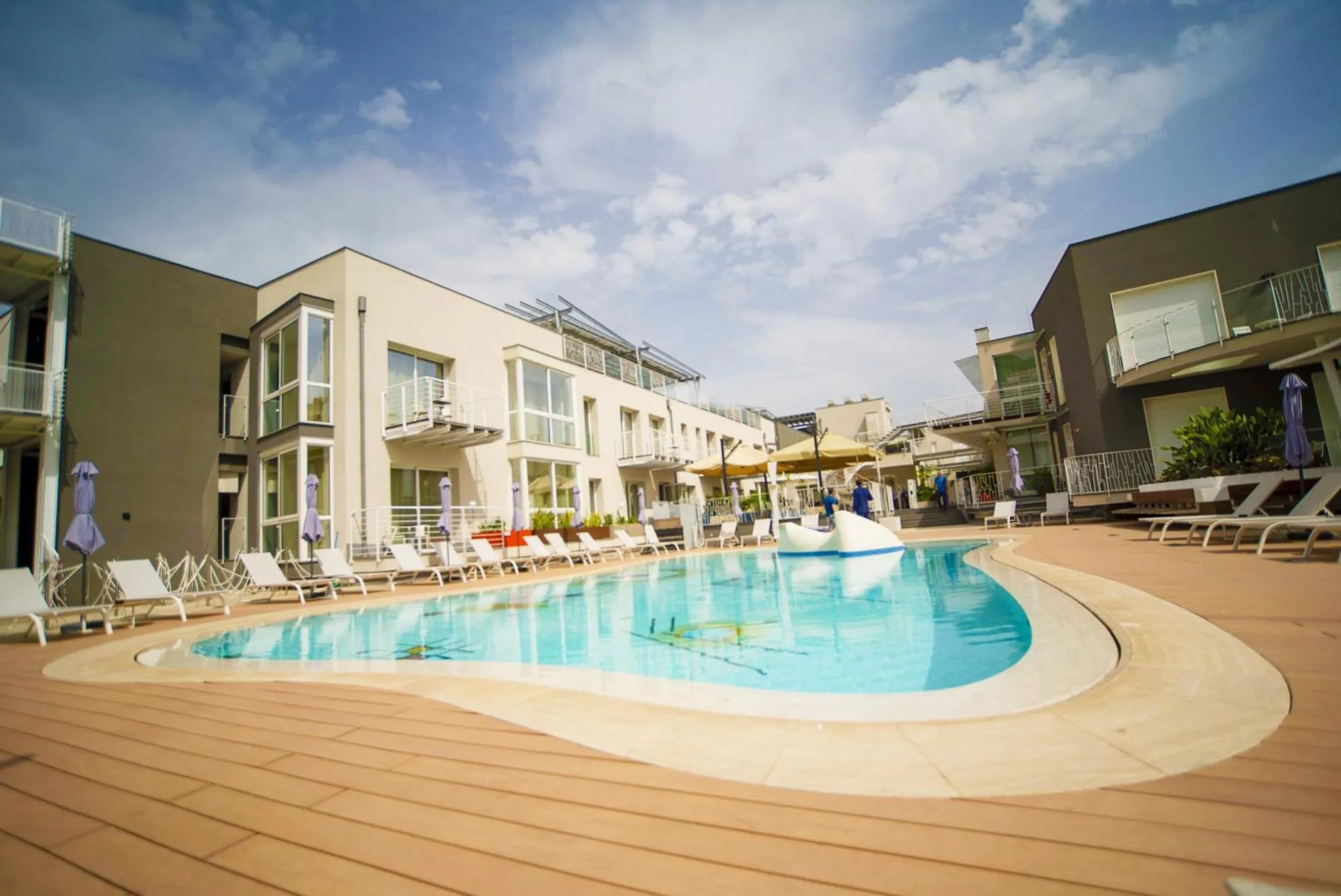 Une piscine bordée d'une terrasse avec des transats et des parasols devant un bâtiment.