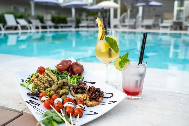 Assiette de tapas et cocktails colorés au bord d'une piscine.