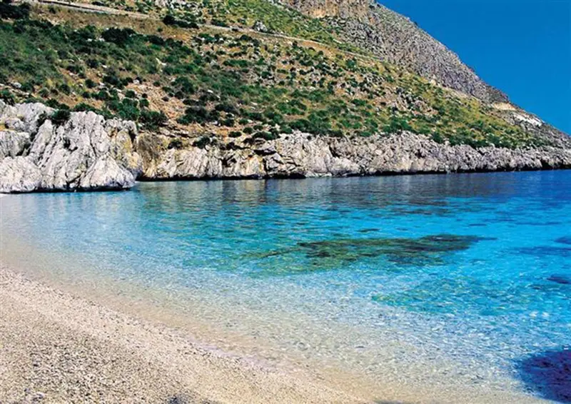 Une plage de galets bordée d'une eau turquoise et d'une côte rocheuse.