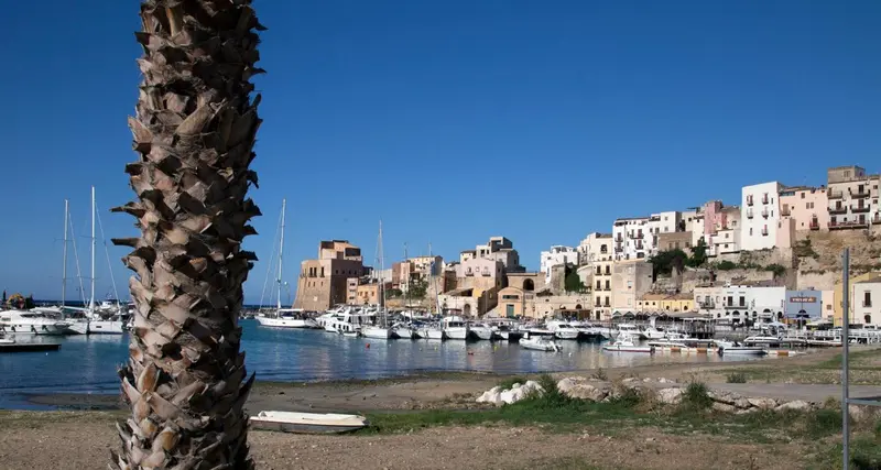 Un port de plaisance ensoleillé avec des bateaux amarrés et des bâtiments colorés en arrière-plan.