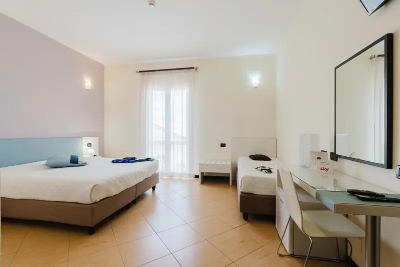 Chambre lumineuse avec deux lits et un bureau près d'une fenêtre.