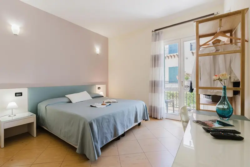 Une chambre lumineuse avec un lit fait et un bureau près d'une porte-fenêtre.