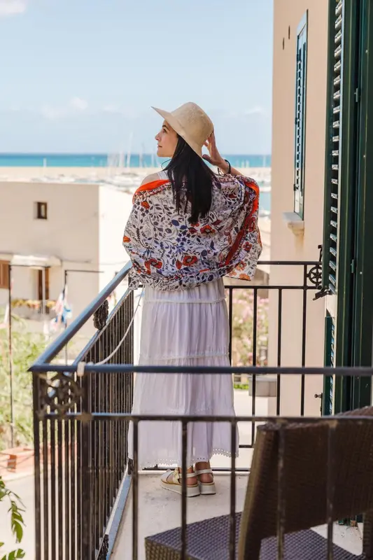 Une femme regarde la mer depuis un balcon fleuri.