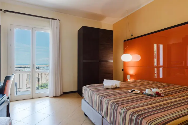 Une chambre lumineuse avec un lit fait et un balcon donnant sur la mer.
