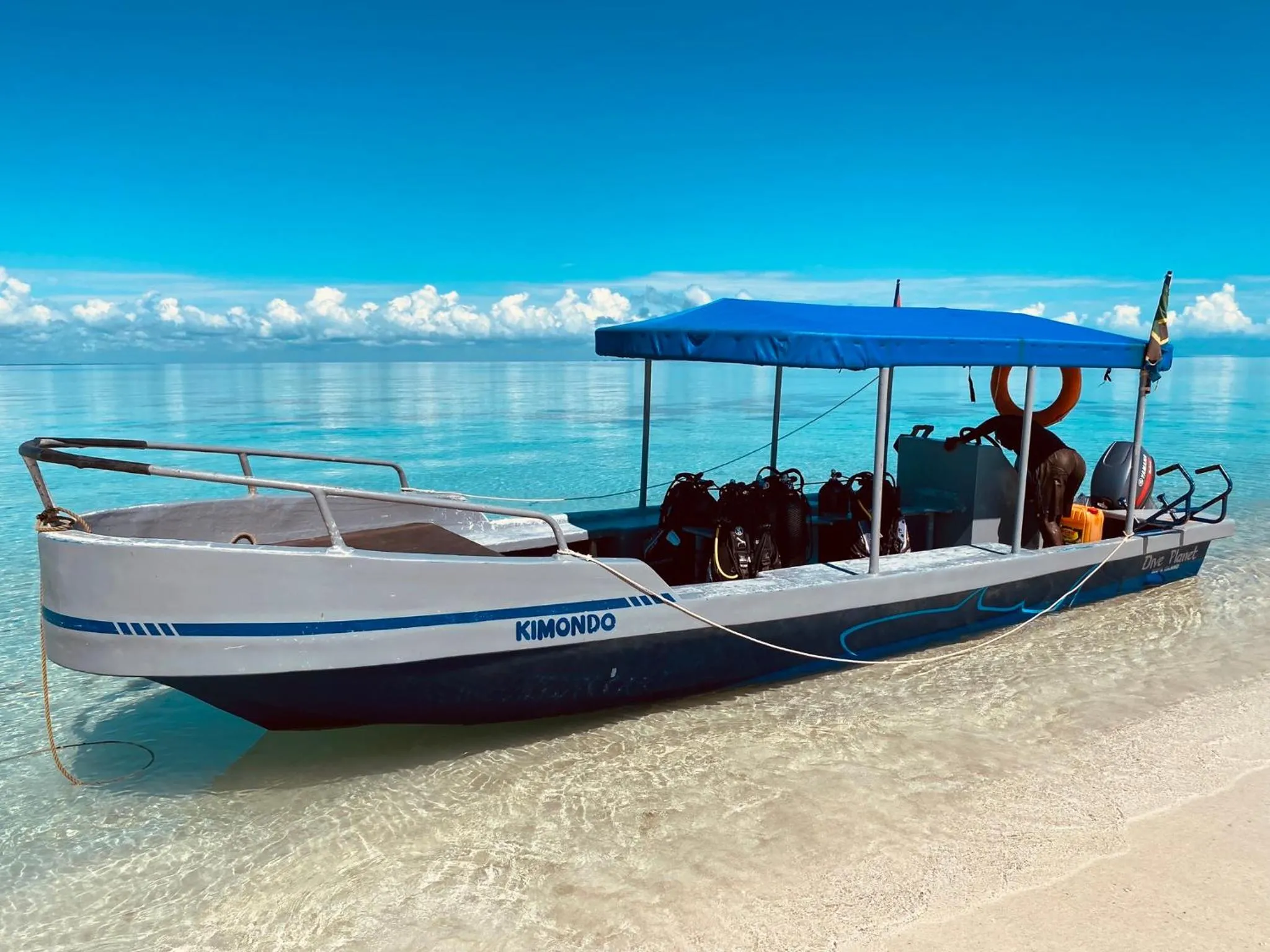 Un bateau de pêche traditionnel est échoué sur une plage de sable blanc sous un ciel bleu nuageux.