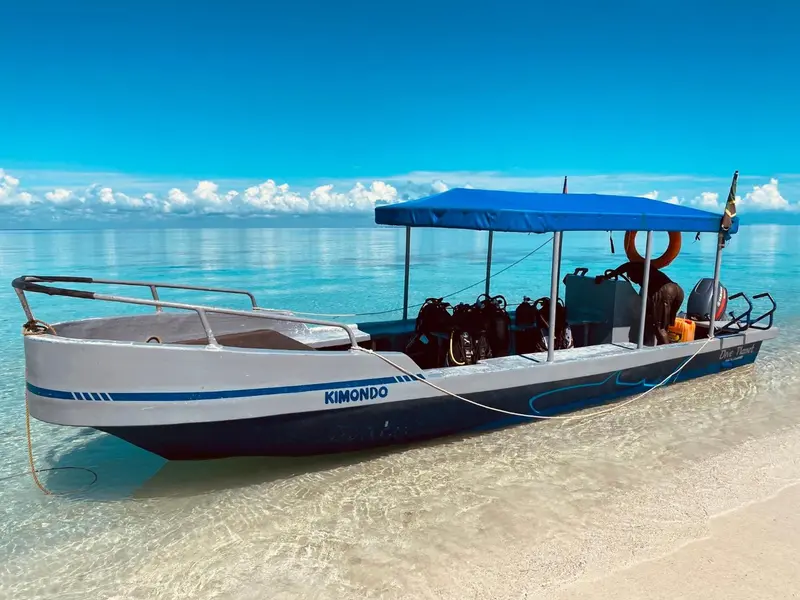 Un bateau de pêche traditionnel est échoué sur une plage de sable blanc sous un ciel bleu nuageux.