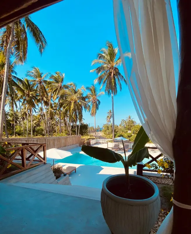 Vue sur une piscine et une végétation luxuriante depuis un espace intérieur.